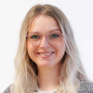 Portrait einer Frau mit langen, blonden Haaren und Brille, freundlich blickend.